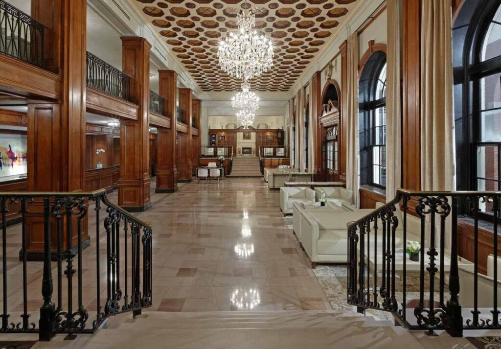 Lord Nelson Hotel & Suites lobby with chandeliers, wood panelling and lounge seating for guests.
